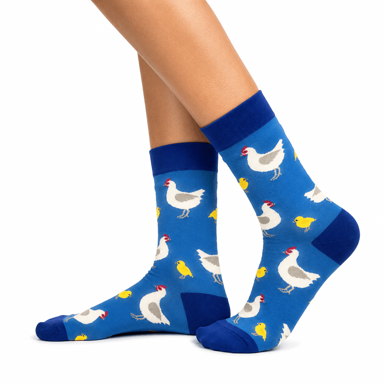 A pair of blue crew socks with a pattern of white chickens, yellow chicks, and red combs, shown on a person's feet against a white background.