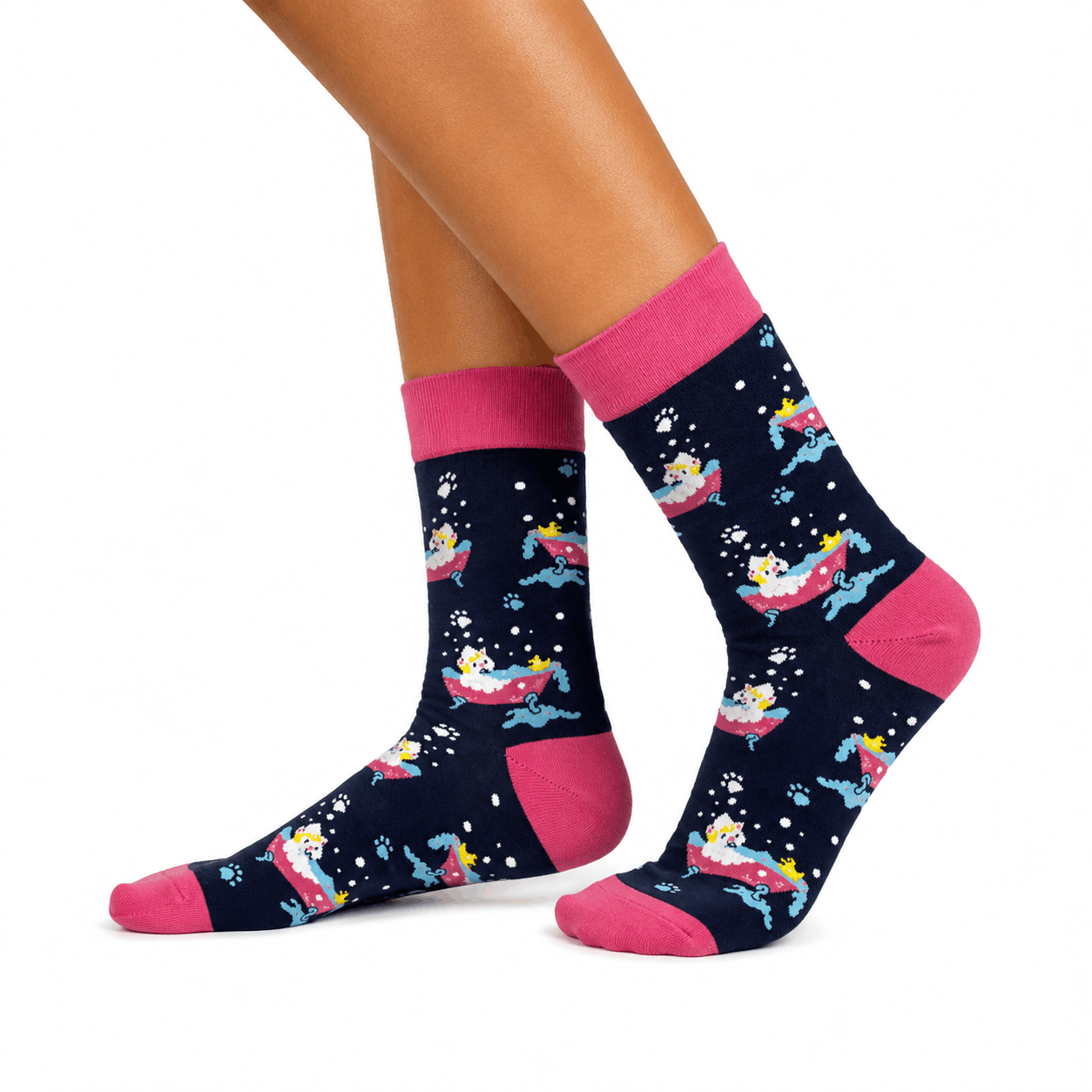 A pair of crew socks worn on a person's feet, shown against a plain white background. The socks have a dark navy blue base with a repeating cartoon pattern of cats in bubble baths, with bright pink cuffs, heels, and toes.