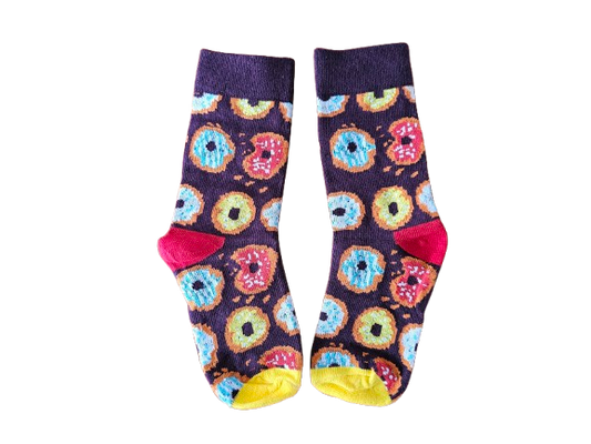 A pair of crew socks with a colorful donut pattern on a dark purple background, featuring bright pink heels and toes with yellow toes, displayed against a plain white background.