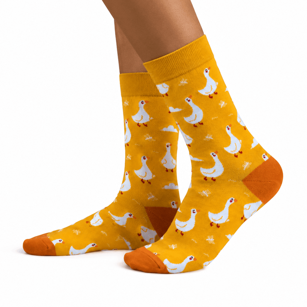 A pair of mustard yellow crew socks with a white goose pattern, shown on a person's feet against a plain white background.