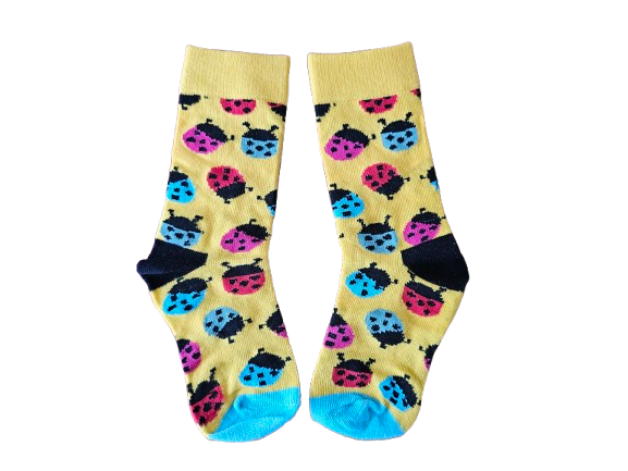 A pair of yellow crew socks with a colorful ladybug pattern, featuring dark navy heels and toes with bright blue soles, shown against a plain white background.
