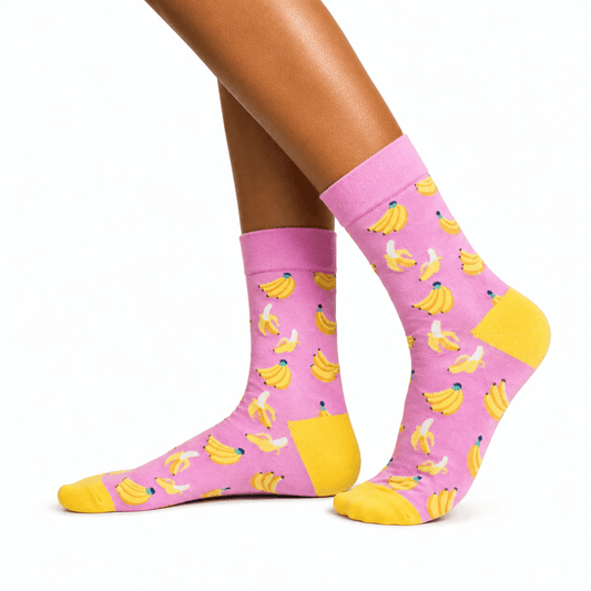 Pink crew socks with a yellow banana print, worn on a model's feet against a white background.