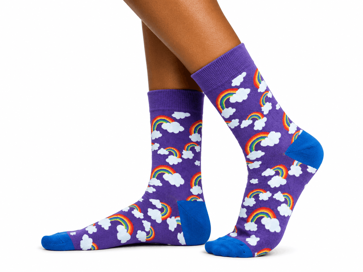 A pair of purple crew socks with a repeating pattern of white clouds and colorful rainbows, worn on a person's feet against a plain white background.