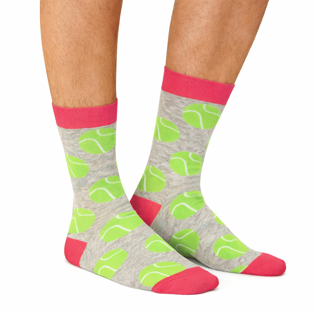Gray socks with tennis ball patterns and pink accents worn by a person on a white background