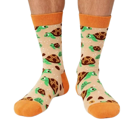 A pair of crew socks worn on a person's feet, featuring a playful pattern of green sea turtles on a light orange background with bright orange cuffs, heels, and toes.