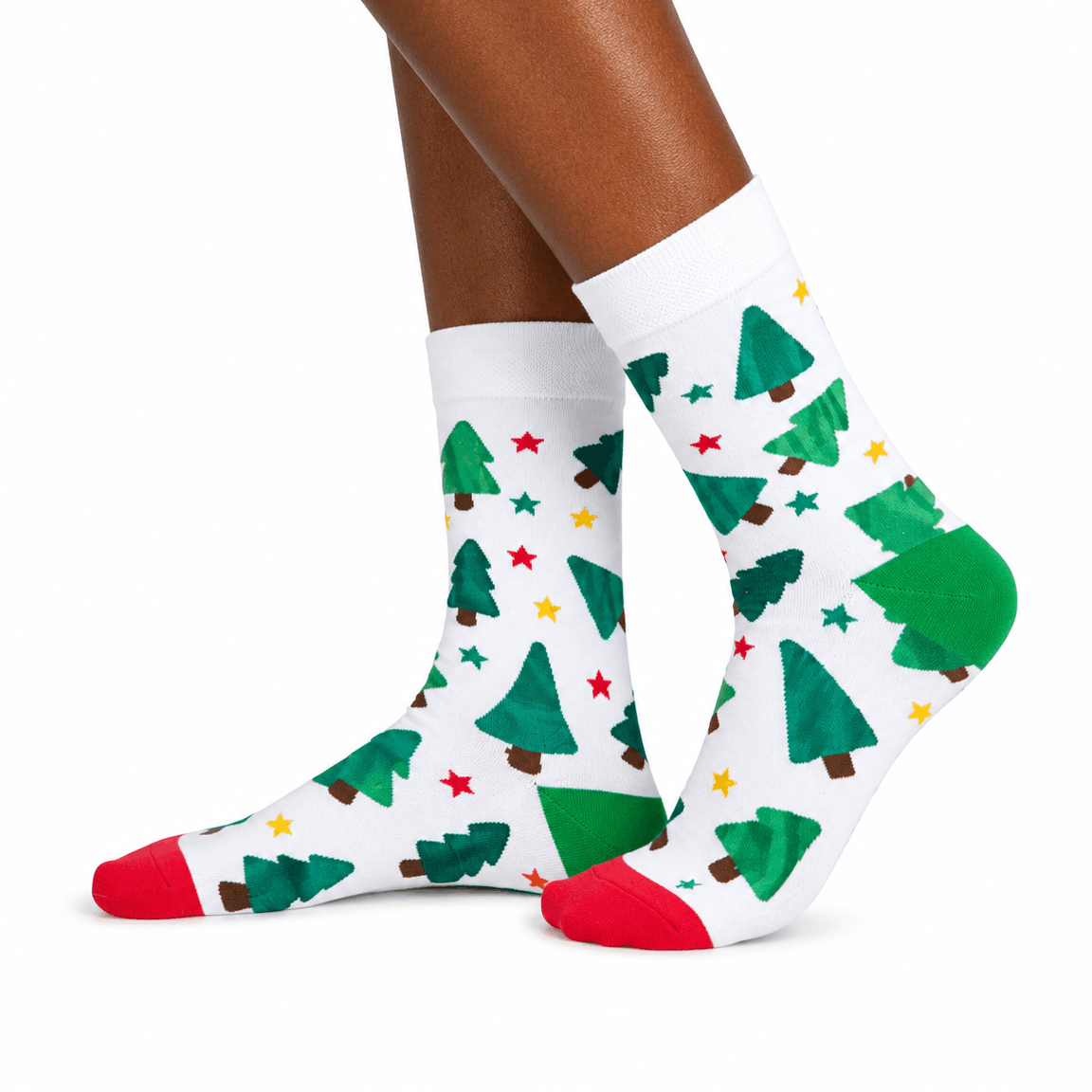 White crew socks with a green Christmas tree and star pattern, featuring red toes and heels, shown on a model's feet against a white background.